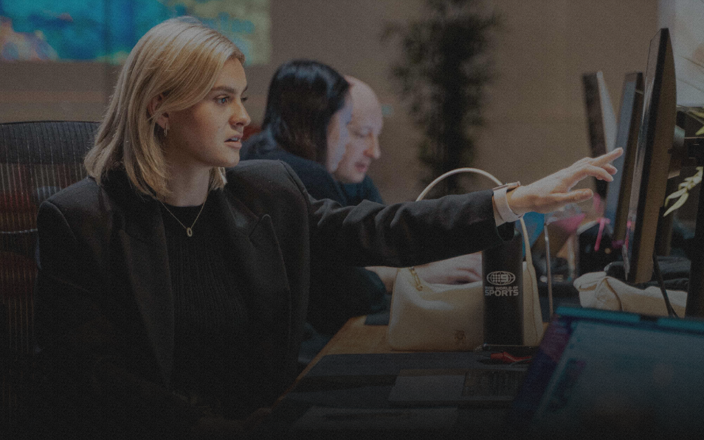 Woman in black jacket pointing at screen.